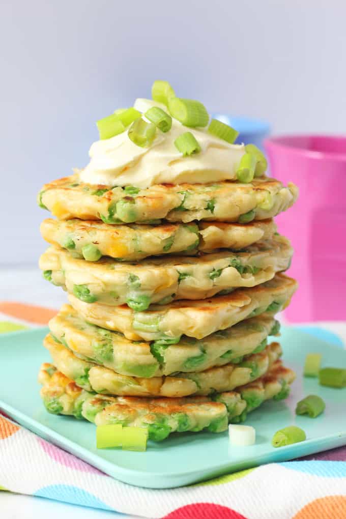 A stack of Pea & Sweetcorn Fritters on a green plate and topped with creme fraiche and spring onions