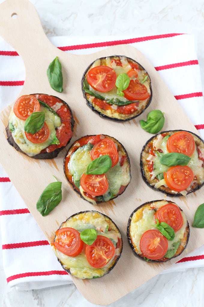 6 aubergine mini pizzas on a wooden chopping board on top of a red and white striped tea towel