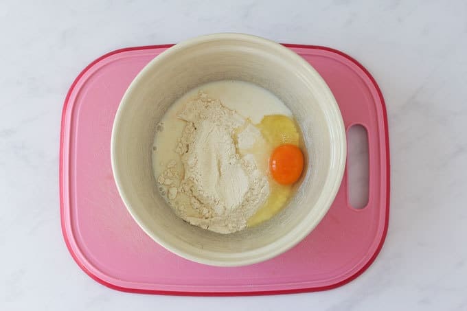 Flour, milk and egg in a bowl on a pink background board