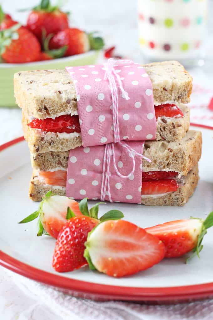 a strawberry and cream cheese sandwich on a plate cut in half and wrapped with a pink polka dot napkin and tied with twine
