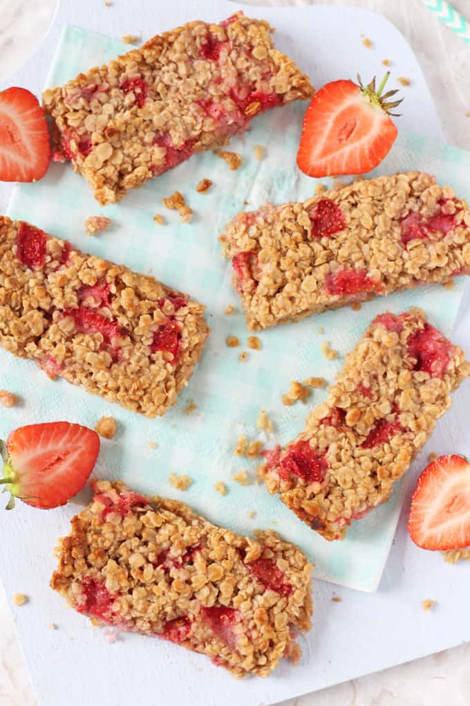 5 Strawberry Oat Bars served on a light blue wooden board with halved strawberries.