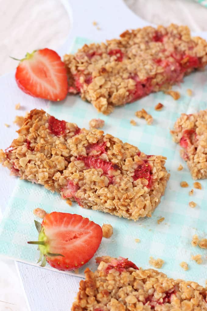 Slices of Strawberry Oat Bars garnished with chopped strawberries on a blue gingham napkin