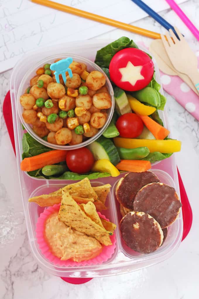 open lunchbox with a salad, cheese, chocolate covered rice cakes, and chips with a dip