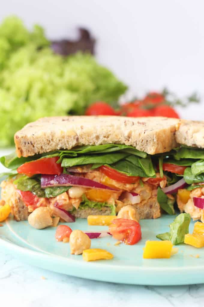 Sriracha Mashed Chickpea Sandwich cut in half to show all the fillings on a light blue plate.