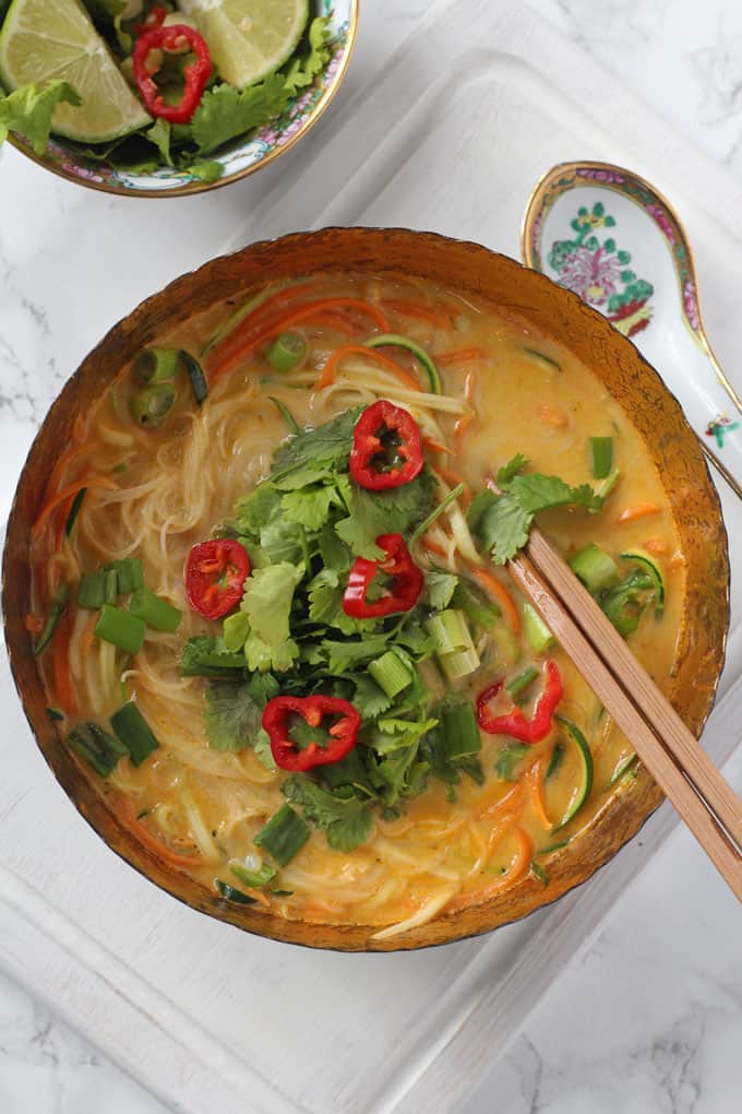 vegetable laksa in a bowl with chopsticks alongside a chinese spoon