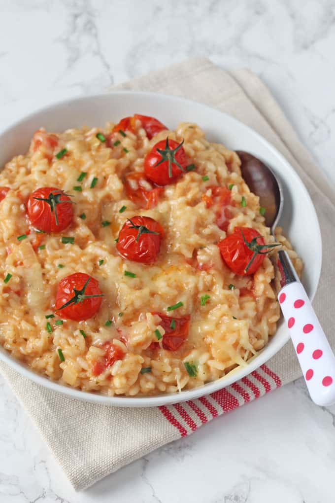 Baked Cheese & Tomato Risotto in a white bowl with a red polka dot spoon on top of a red and white tea towel