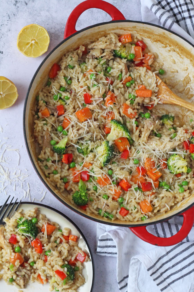 Leftover Roast Chicken Risotto in a large red ovenproof dish next to a serving of the risotto on a plate.