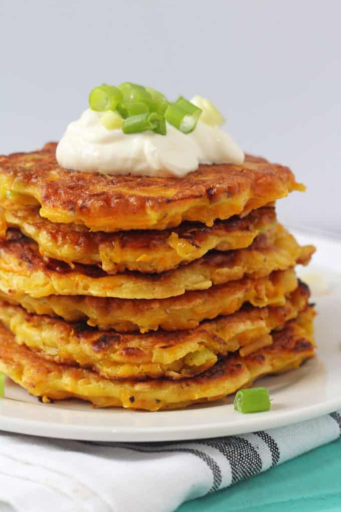 6 butternut squash fritters stacked on a white plate and topped with creme fraiche and spring onion