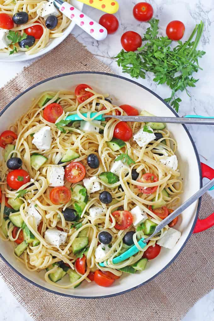Greek Salad Linguine served in a red cast iron [an on top of a hessian mat with a set of tongs rest on top