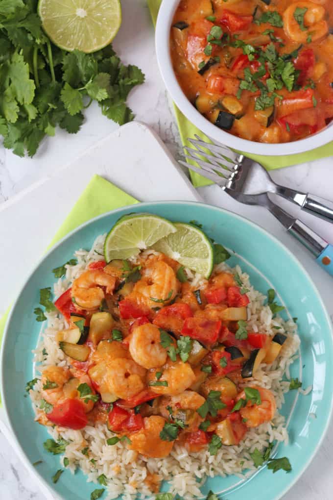 Thai Red Prawn Curry served on a blue plate with rice and two lime wedges