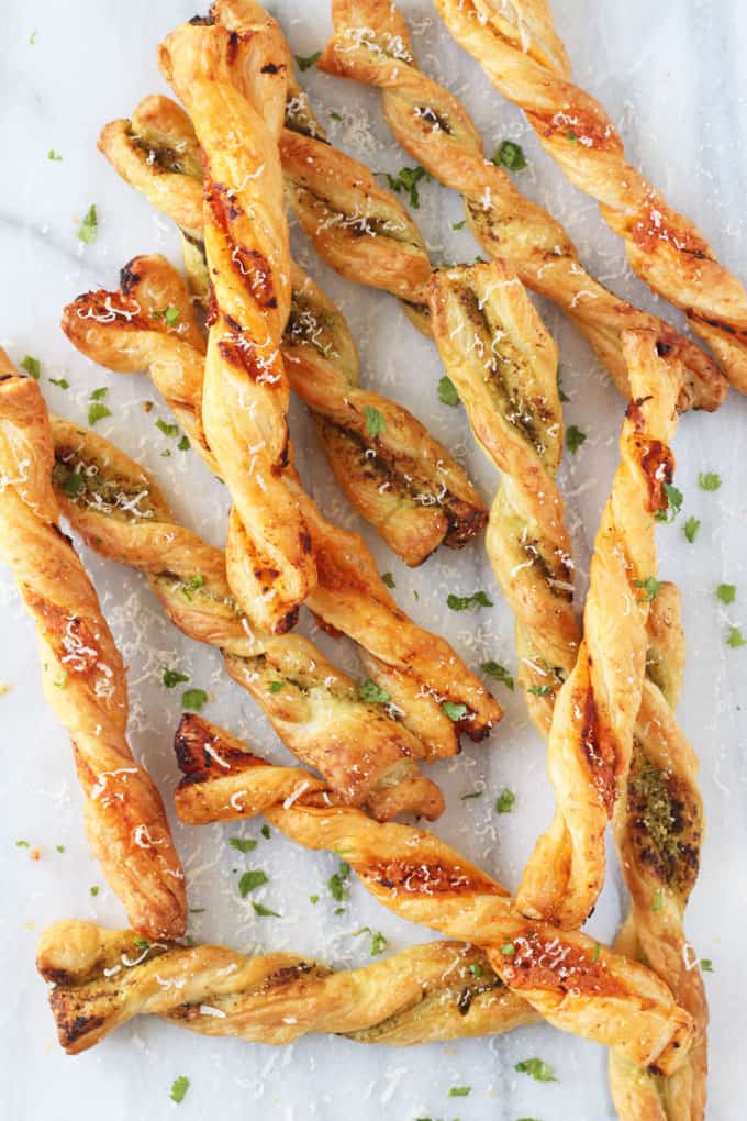 Pesto Parmesan Pastry Straws on a white marble background garnished with grated parmesan and chopped fresh parsely