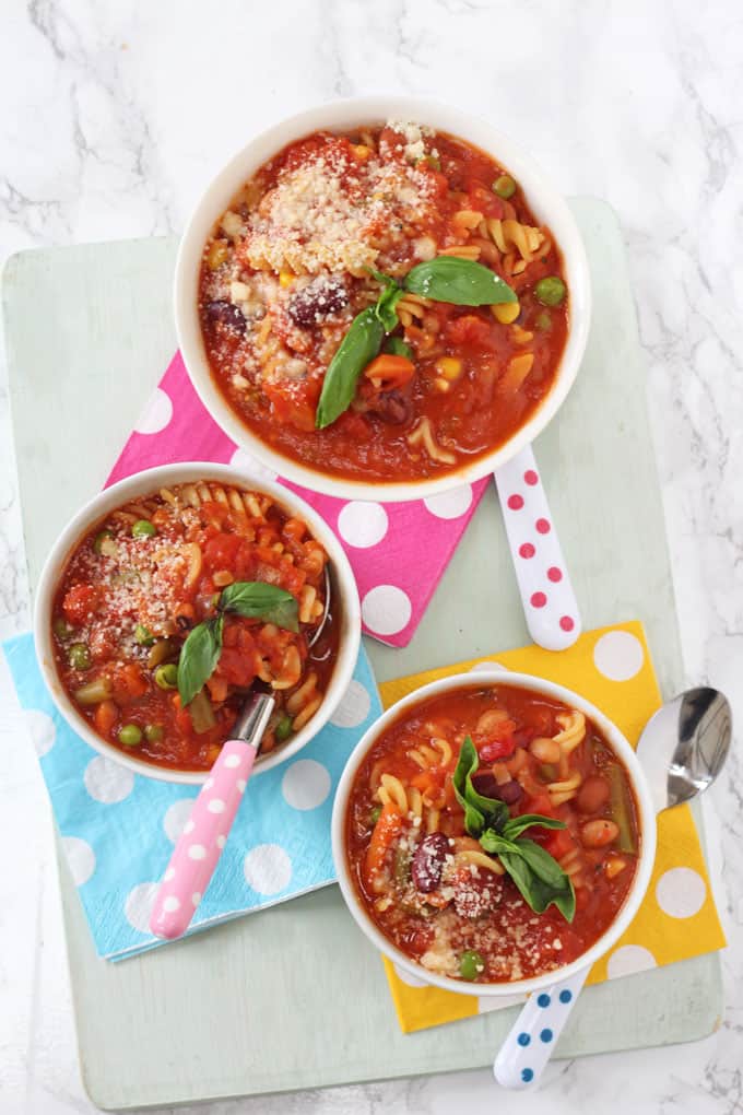  3 bowls of easy minestrone soup on multi colored polka dot napkins on top of a wooden chopping board