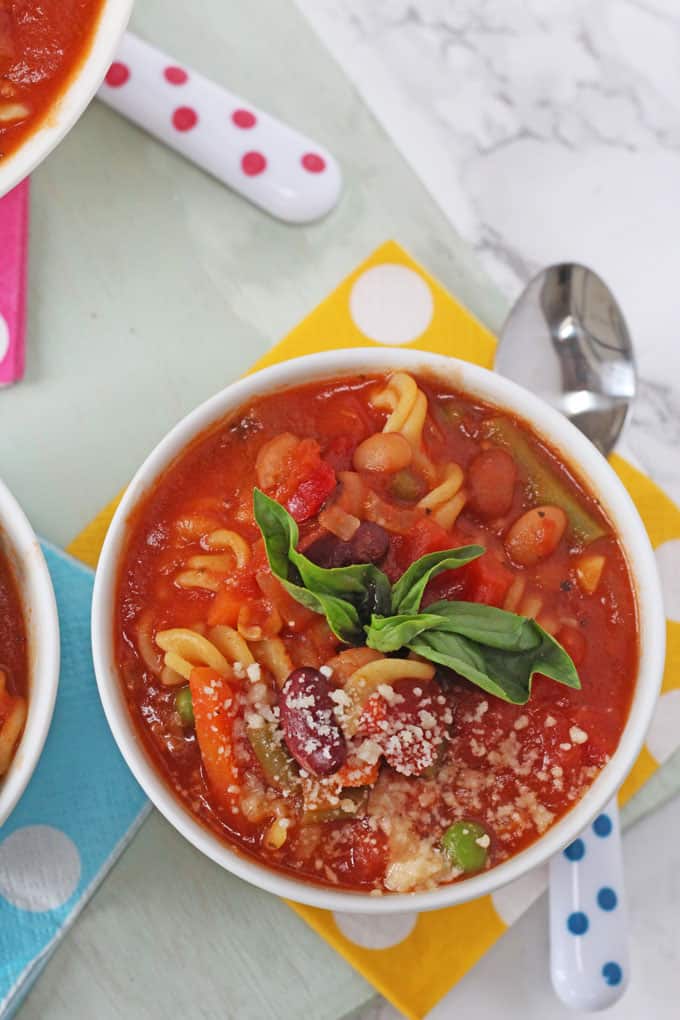 close up of the minestrone soup in a white bowl topped with basil & grated parmesan