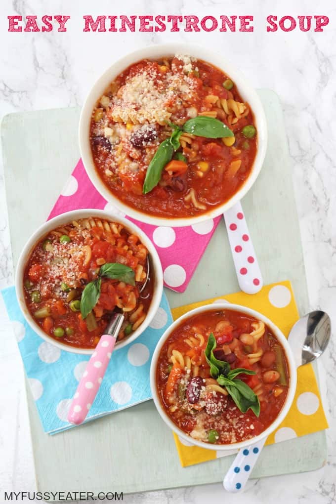 1 large bowl and two small bowls of Easy Minestrone Soup on top of a light blue chopping board with colourful spoons.