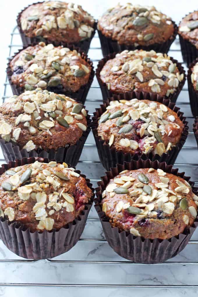 Berry Breakfast Muffins in brown muffin cases on a cooling rack topped with oats and seeds