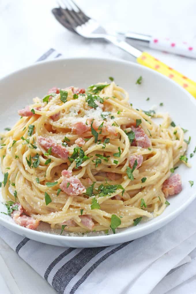 Spaghetti Carbonara in a bowl, garnished with fresh chopped basil and finely grated parmesan cheese