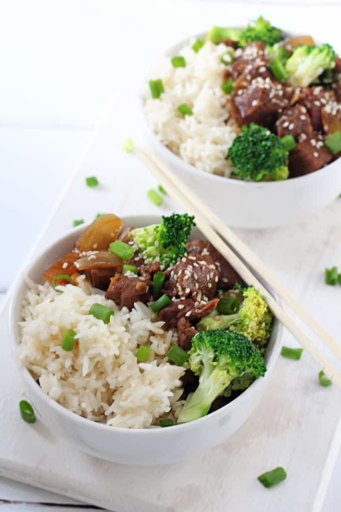 beef & broccoli with rice and topped with sesame seeds in a white bowl with chopsticks resting on the bowl