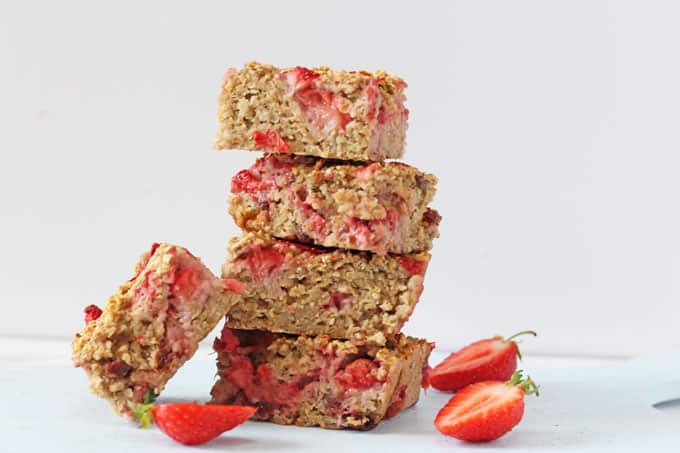 Strawberry quinoa breakfast bars, cut into squares and stacked, with fresh strawberry slices in the foreground