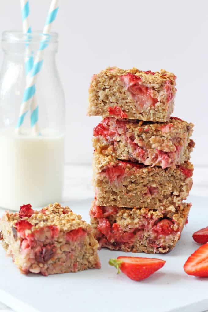 strawberry quinoa breakfast bars, sliced strawberries stacked up next to a bottle of milk with two straws in it 