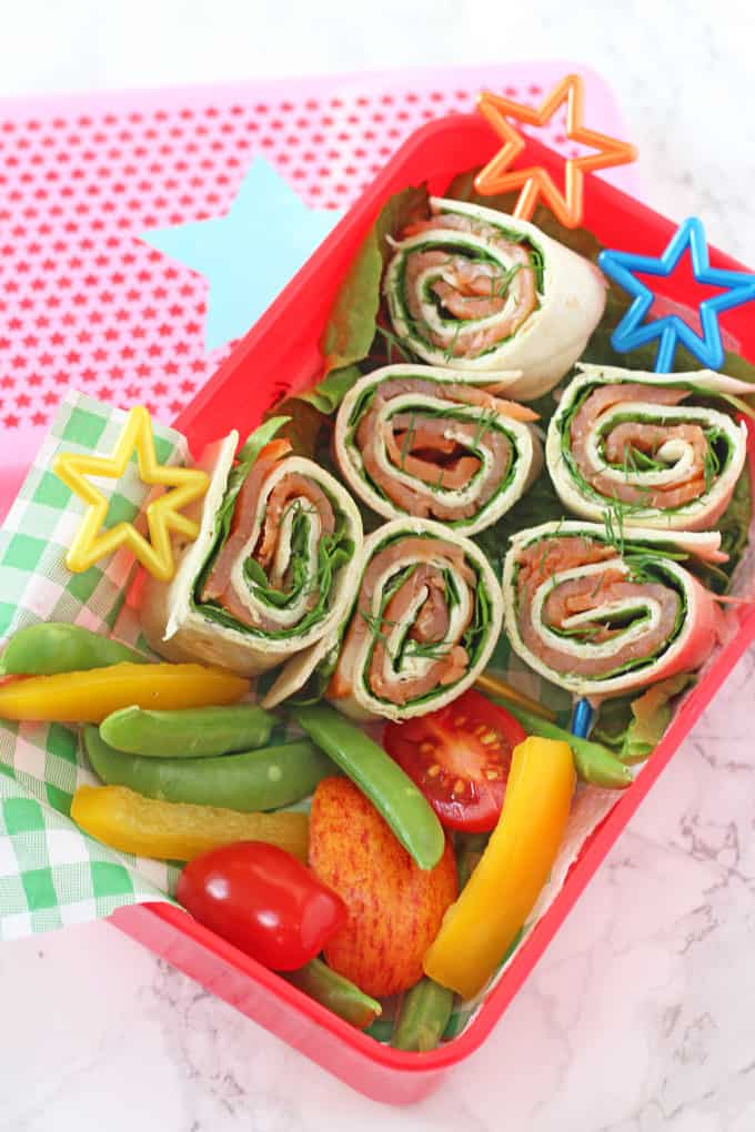 Salmon, cream cheese and spinach pinwheels in a lunch box with sugar snap peas, chopped yellow peppers and cherry tomatoes.