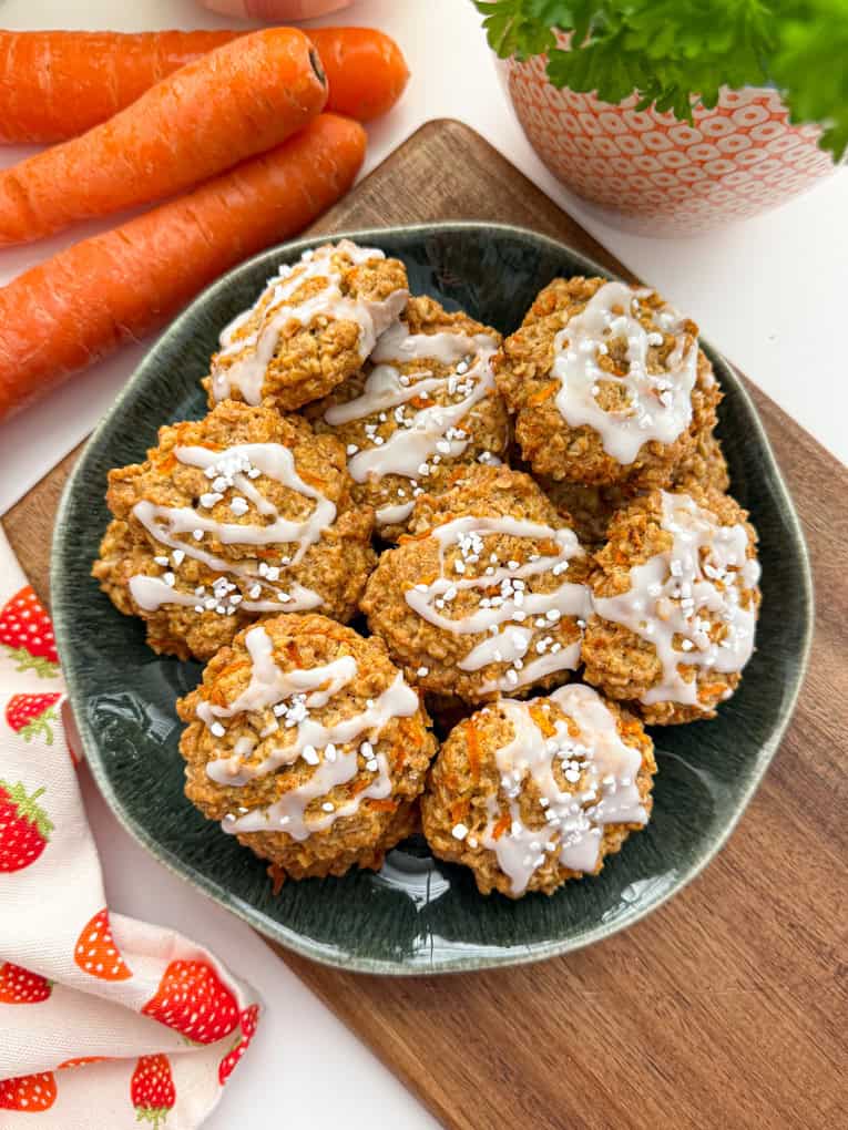 Healthy Carrot Cake Cookies for Kids arranged in a green bowl on a wooden chopping board with some carrots in the background.
