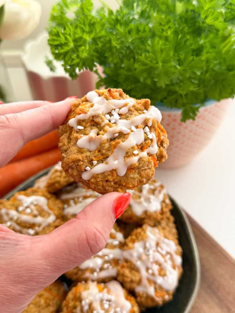 A close up shot of one of the baked carrot cake cookies being held by a female hand.