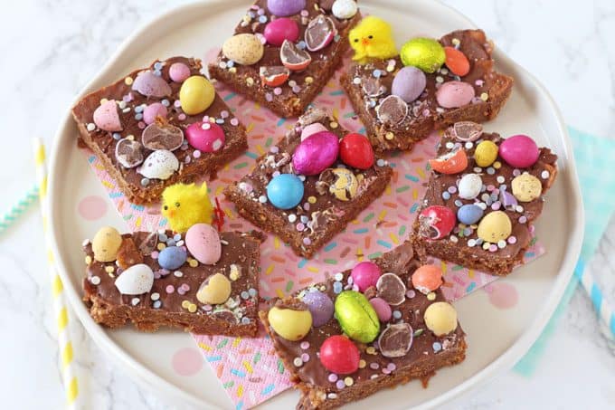 Easter Cornflake Crunch served on a cake stand, decorated with confetti sprinkles and Smartie Mini Eggs