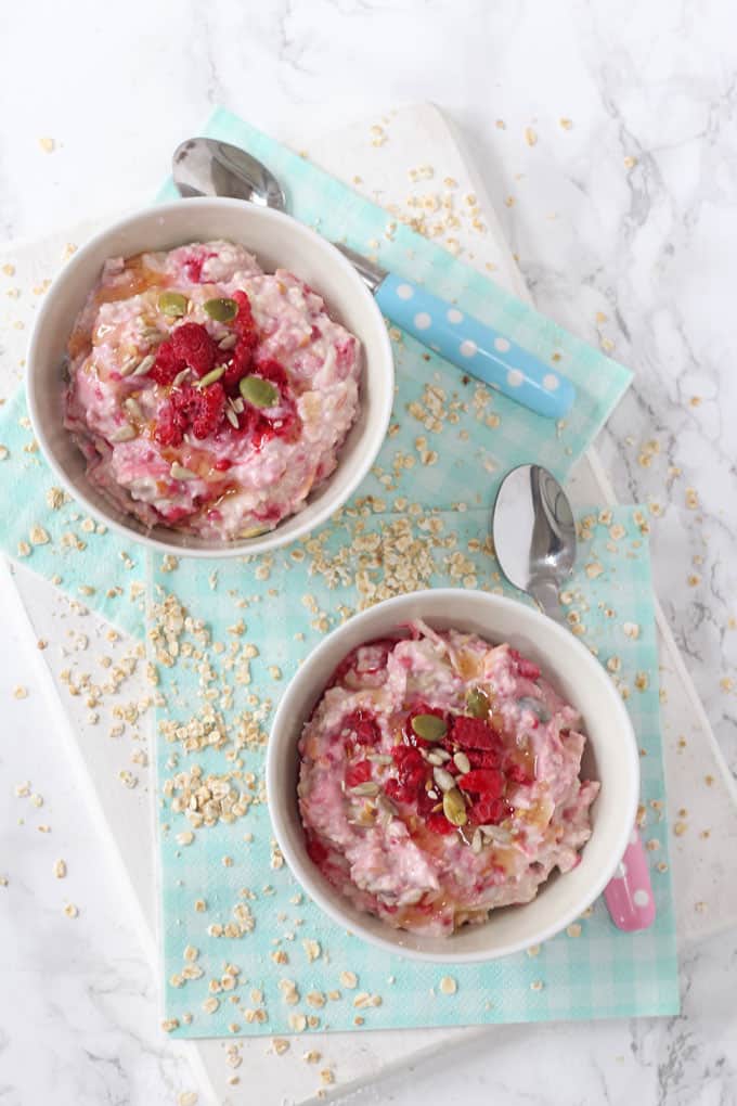 2 bowls of bircher muesli for kids shown sitting on top of a pale blue napkin photographed from above