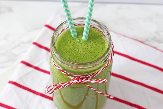 dairy free smoothie packed with kale, pineapple, mango and melon in a glass jar with two striped straws in it.
