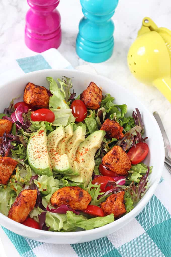 Smoked Paprika Chicken Salad served in s white bowl and garnished with sliced avocado and a light dusting of paprika.