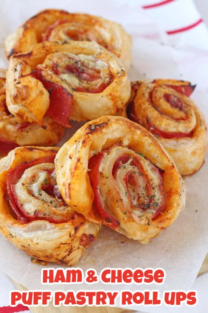 Ham & Cheese Puff Pastry Roll Ups stacked on a sheet of parchment paper on top of a red and white striped tea towel.