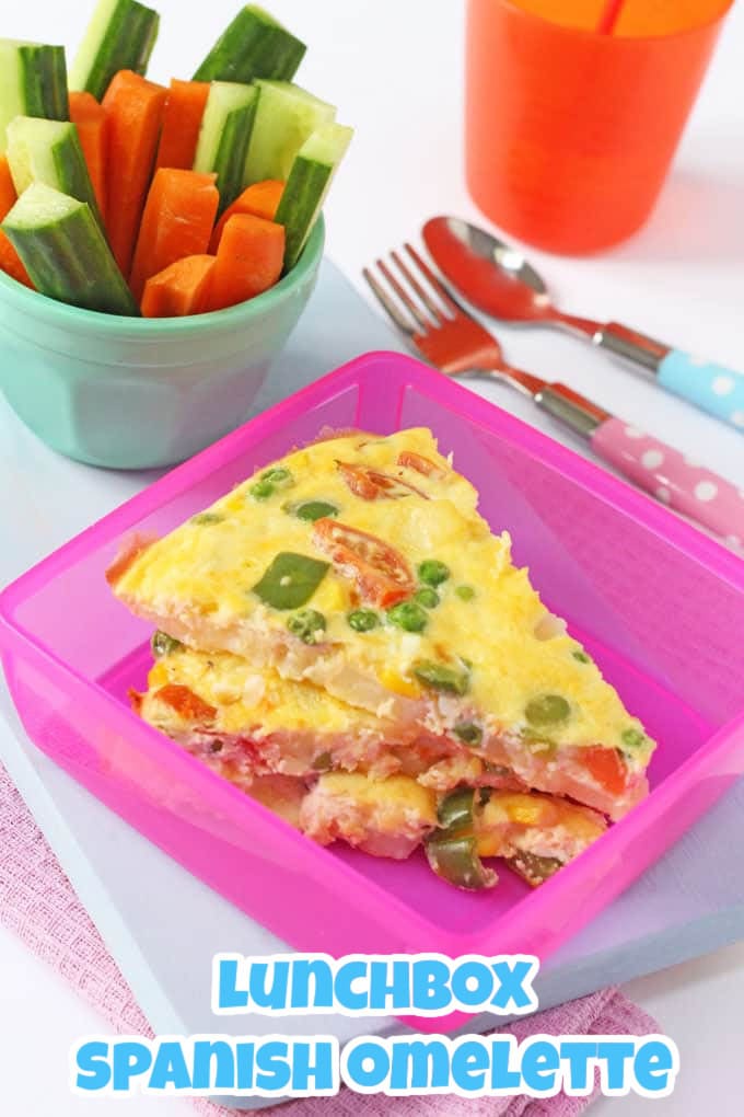 Lunchbox Spanish Omelette cut into triangles and stored in a pink tupperware box with a small blue ramekin of crudites in the background.