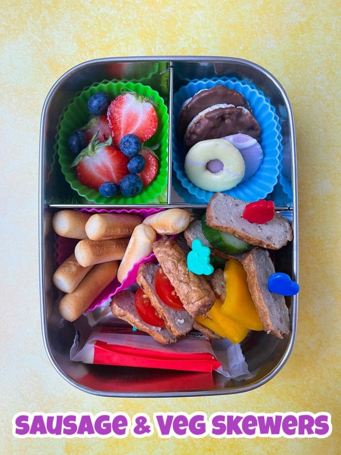 Sausage and veg skewers on mini food skewers for kids from pick plates, with mini breadsticks, chopped strawberries, blueberries and mini biscuits.