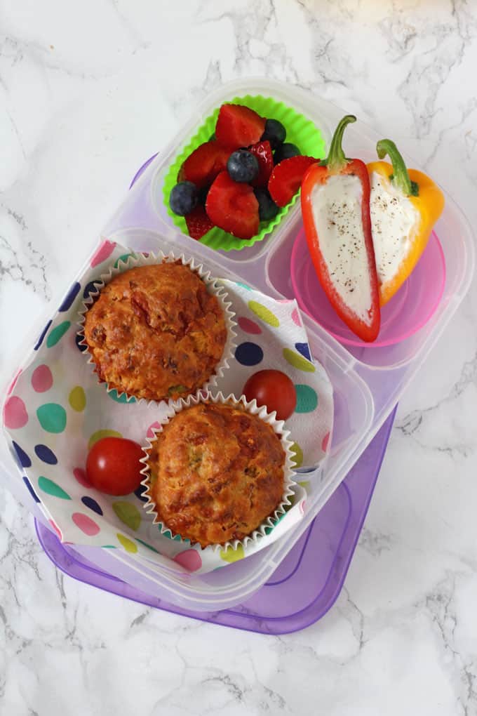 Pizza Lunchbox Savoury Muffins served in a lunchbox alongside fresh strawberries, blueberries and mini peppers stuffed with cream cheese.