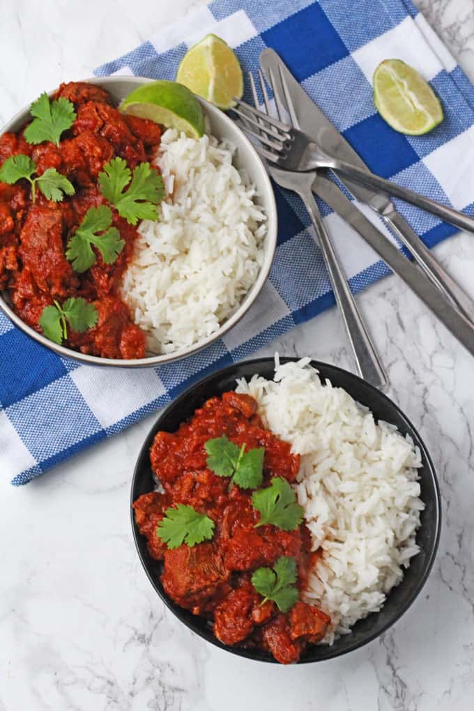 Easy slow cooker lamb curry served on a white bowl accompanied by white rice and garnished with coriander.