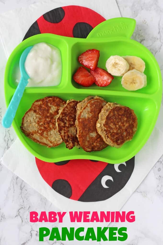Baby Weaning Pancakes in a green apple shaped divided plate for kids with a small portion of yogurt and some chopped banana and strawberries.