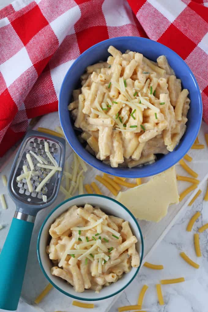 Slow Cooker Mac & Cheese served in a small bright blue bowl and garnished with chopped chives and grated cheese.