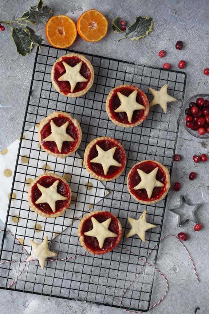 cranberry & orange pies on a wire rack with some oranges, cranberries and holly leaves in the background