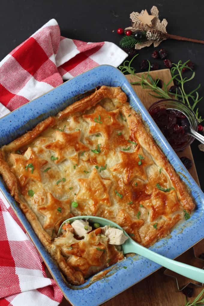 Turkey, Cranberry & Brie Pie in a blue ovenproof dish on a wooden chopping board with a side of cranberry sauce.