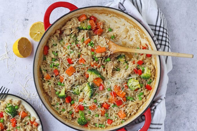 Leftover roast chicken risotto in a large red skillet with a wooden spoon and some chopped lemon in the background