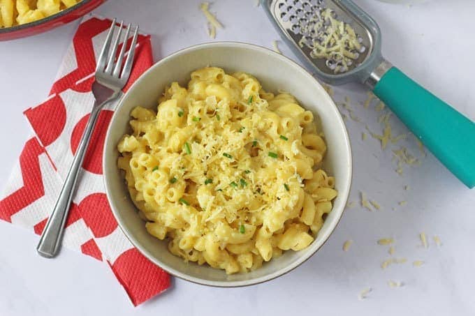 A big bowl of hidden vegetable macaroni cheese with grated cheese and a cheese grater