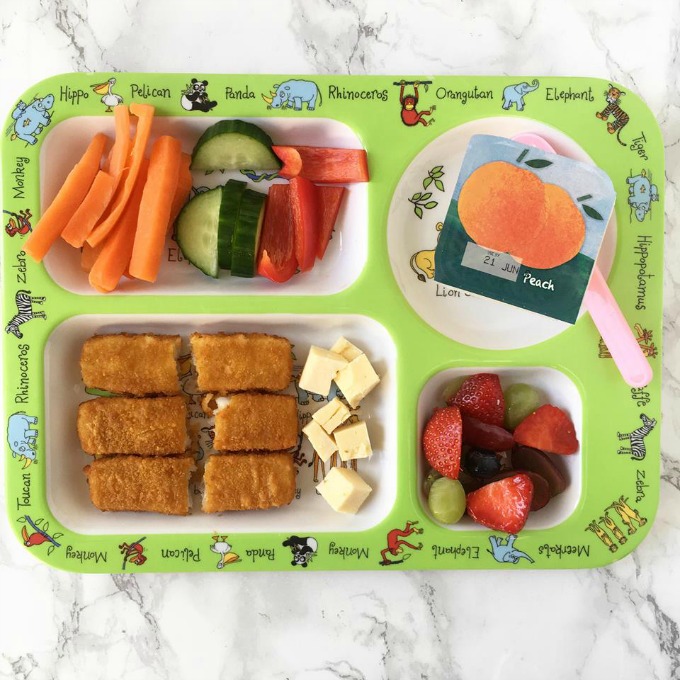 Green kids plate with fish fingers, cheese and other items for dinner