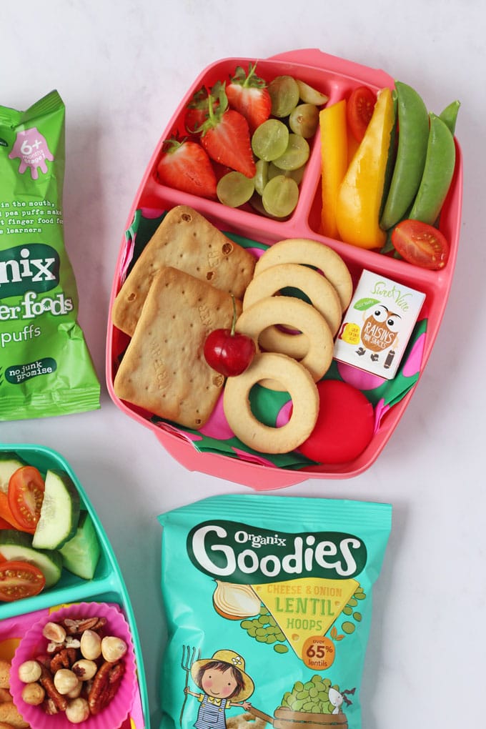 Pink lunch box filled with fruit, vegetables and crackers