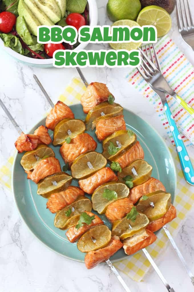 3 BBQ Salmon Skewers on large stainless steel skewers on a light blue plate with side salads in the background.