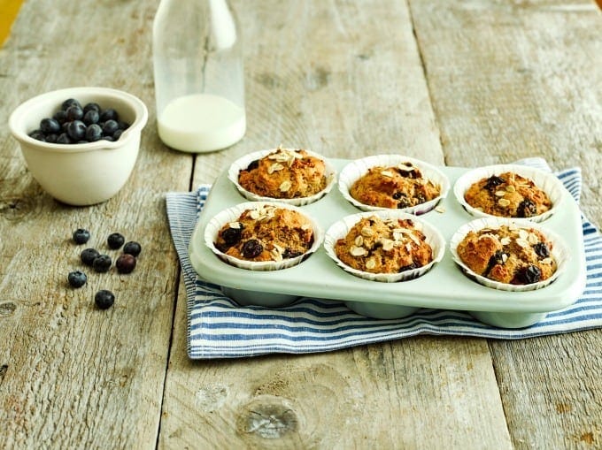 Fruity breakfast muffins in a green silicone muffin tin with a bowl of blueberries in the background and a glass of milk