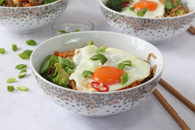Veggie noodle stir fry served in a white bowl with a fried egg on top
