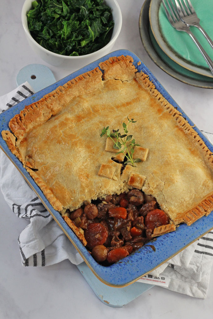 The cooked pie ready to serve next to some plates and a bowl of freshly cooked greens