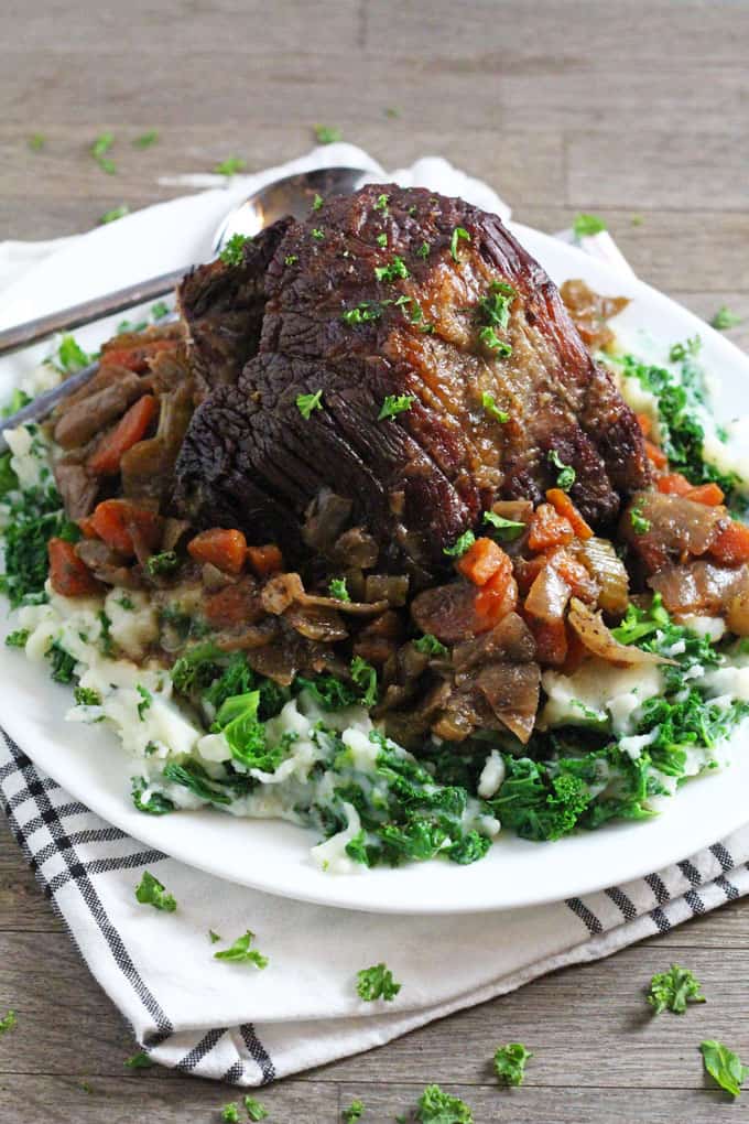 slow cooked beef brisket served on a white plate on a bed of kale mashed potato