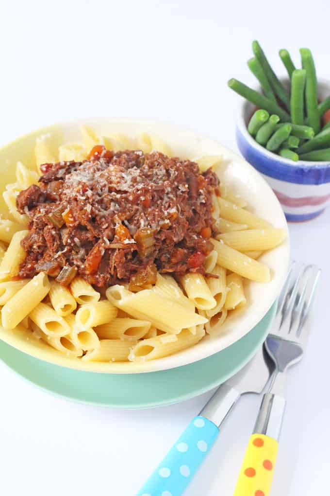 easy slow cooker ragu served on top of cooked penne pasta with a side of cooked breen beans