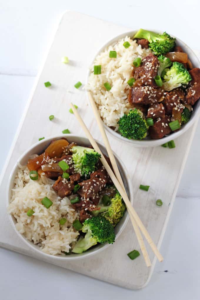 slow cooker beef & broccoli served in two white bowls with white rice on a chopping board with a set of chopsticks